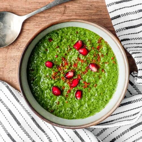 A small bowl of Zhoug Save with a spoon. Garnished with red pepper flakes and fresh pomegranate seeds.