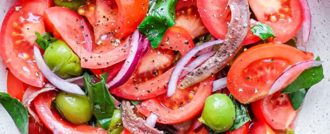 A bowl of Tomato salad with olives, capers, red onion, anchovies and fresh basil.