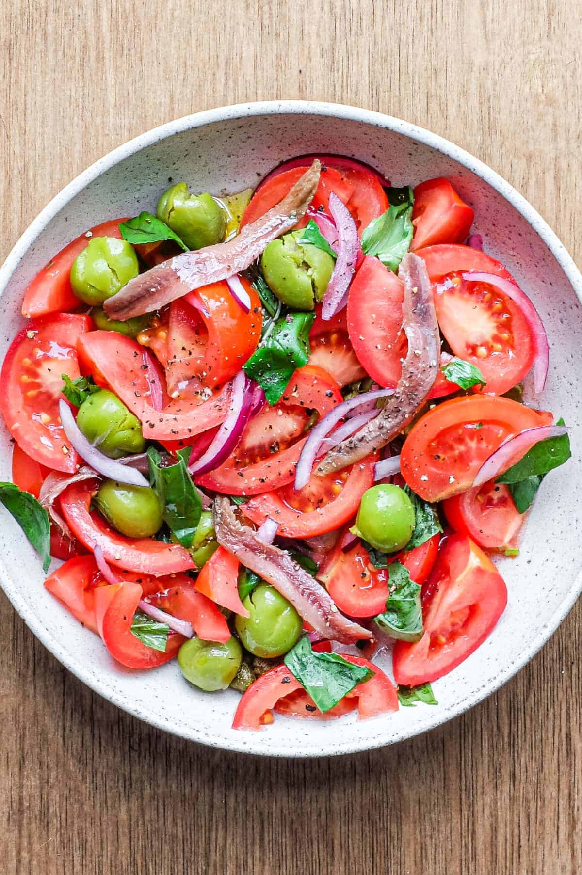 A bowl of Tomato salad with olives, capers, red onion, anchovies and fresh basil.