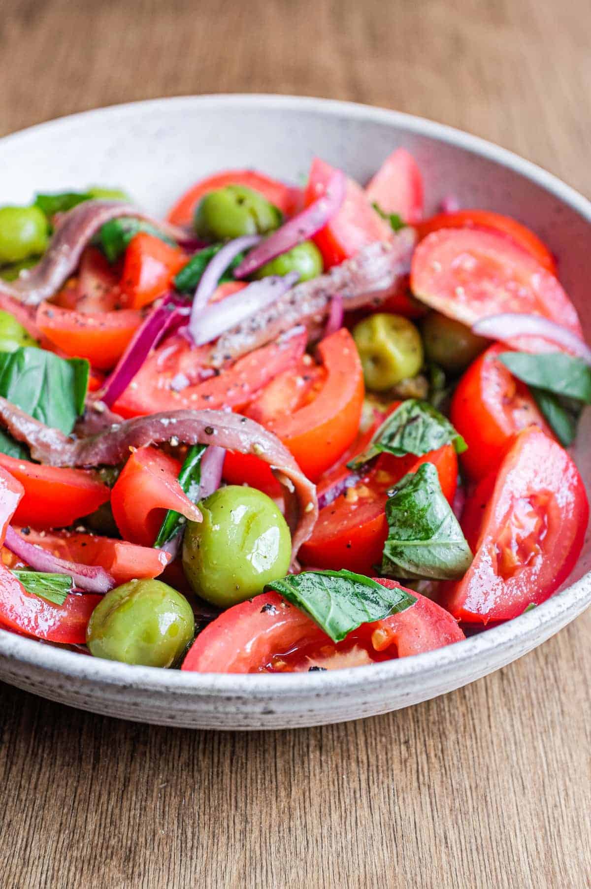 A bowl of Tomato salad with olives, capers, red onion, anchovies and fresh basil.