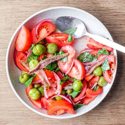 A bowl of Tomato salad with olives, capers, red onion, anchovies and fresh basil.