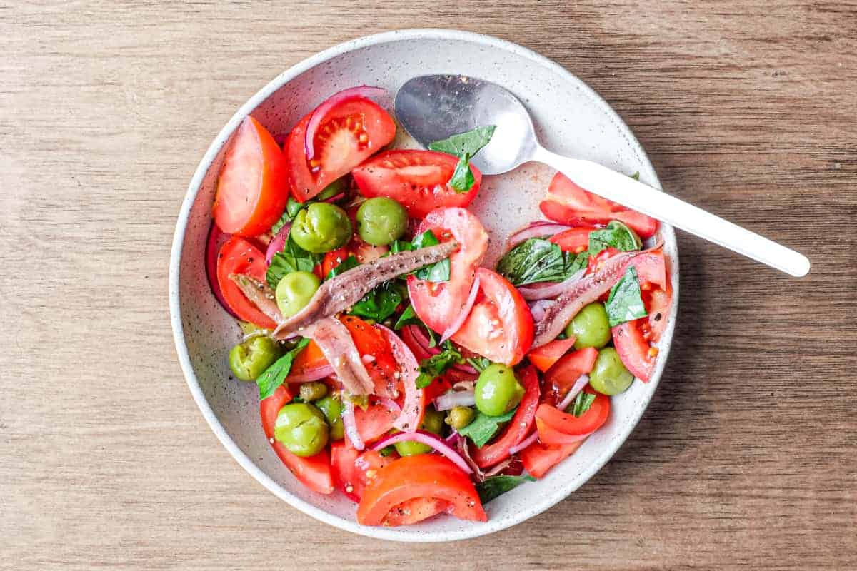 A bowl of Tomato salad with olives, capers, red onion, anchovies and fresh basil.