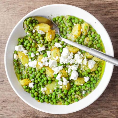 A bowl of Arakas Latheros (Greek Peas) garnished with feta cheese. A serving spoon sits in the bowl.