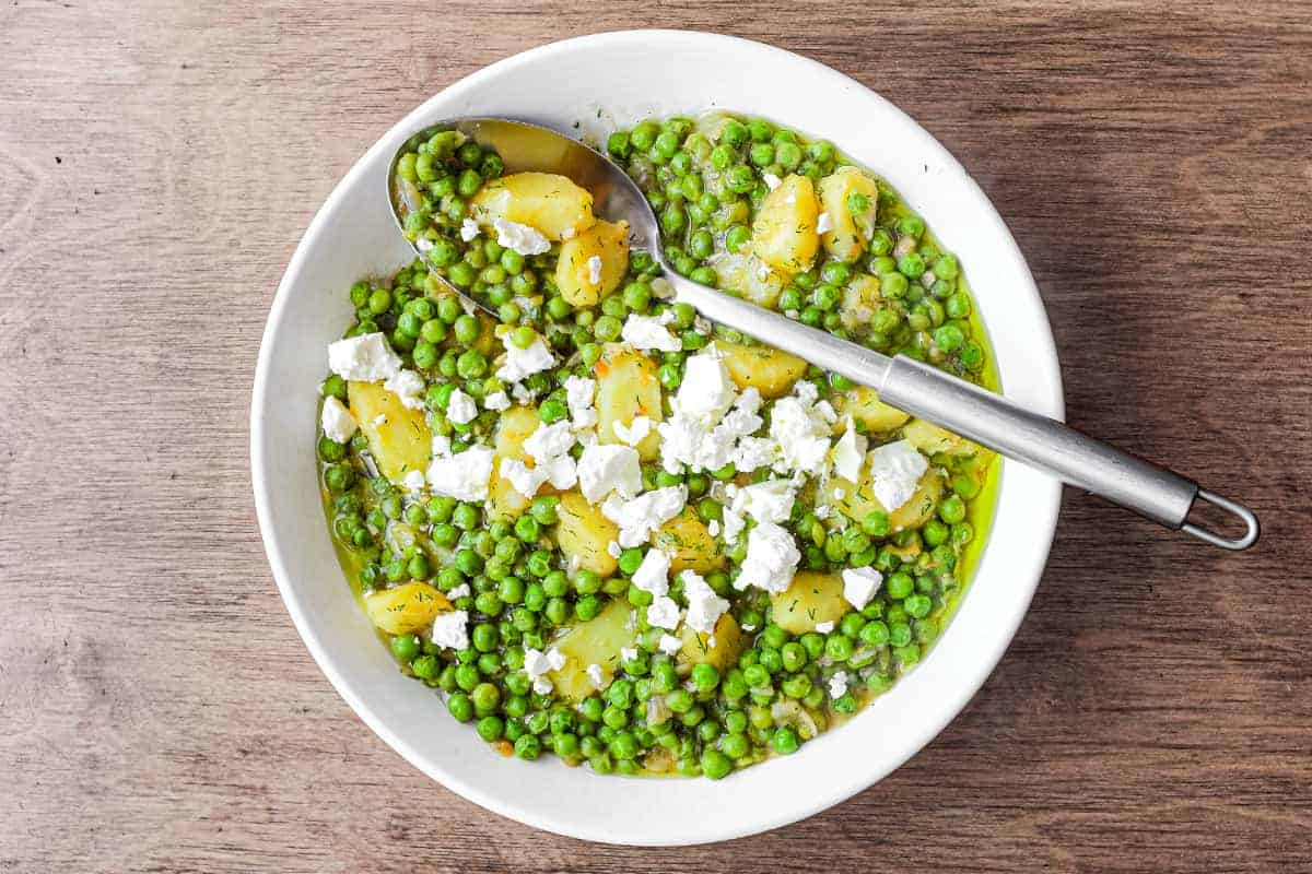 A bowl of Arakas Latheros (Greek Peas) garnished with feta cheese. A serving spoon sits in the bowl.