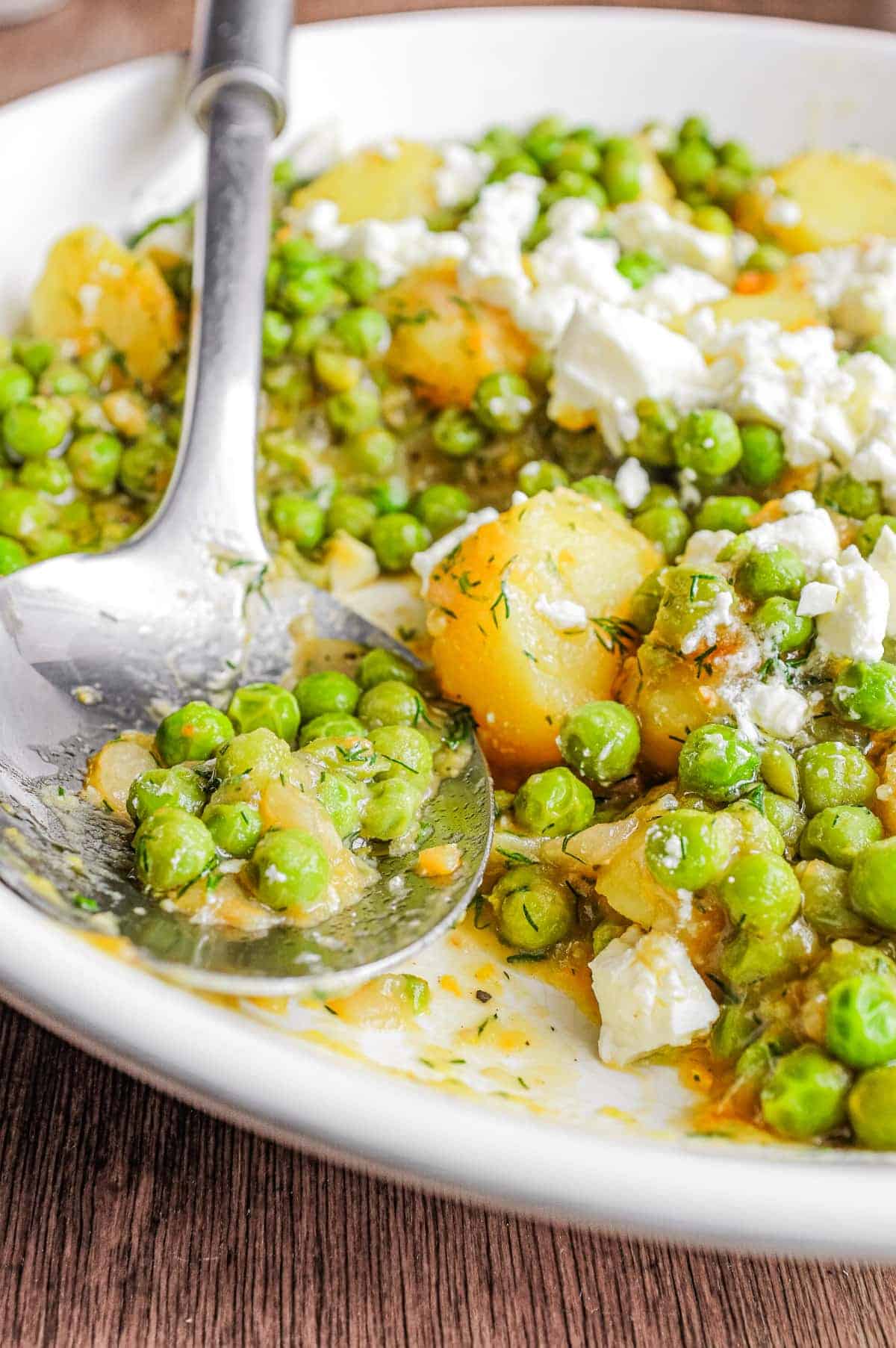 A bowl of Arakas Latheros (Greek Peas) garnished with feta cheese. A serving spoon sits in the bowl.