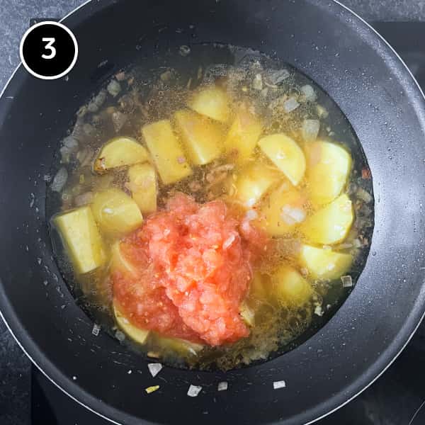 Potatoes in stock/broth with freshly grated tomato in a pan.