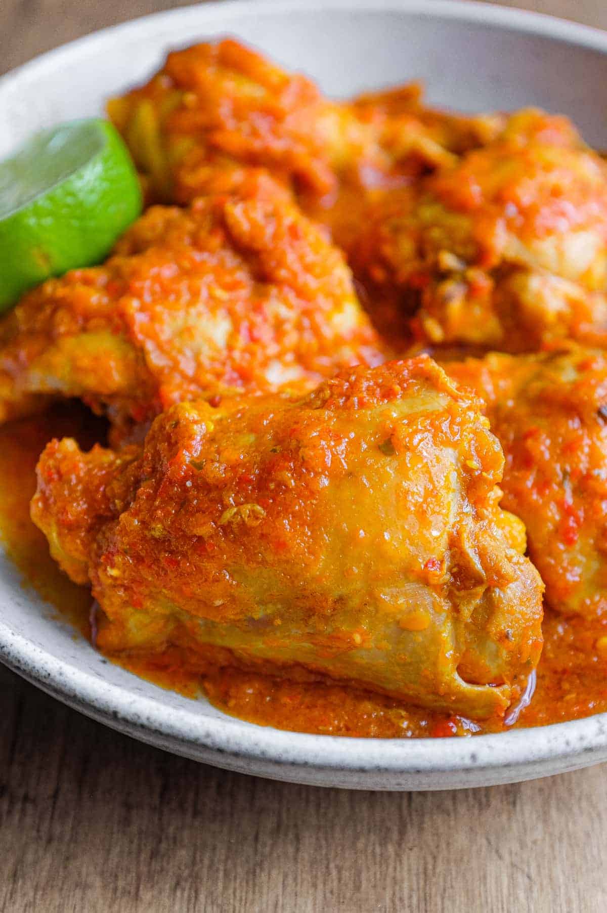 A bowl of Indonesian Ayam Rica Rica. A lime segment sits alongside as a garnish.