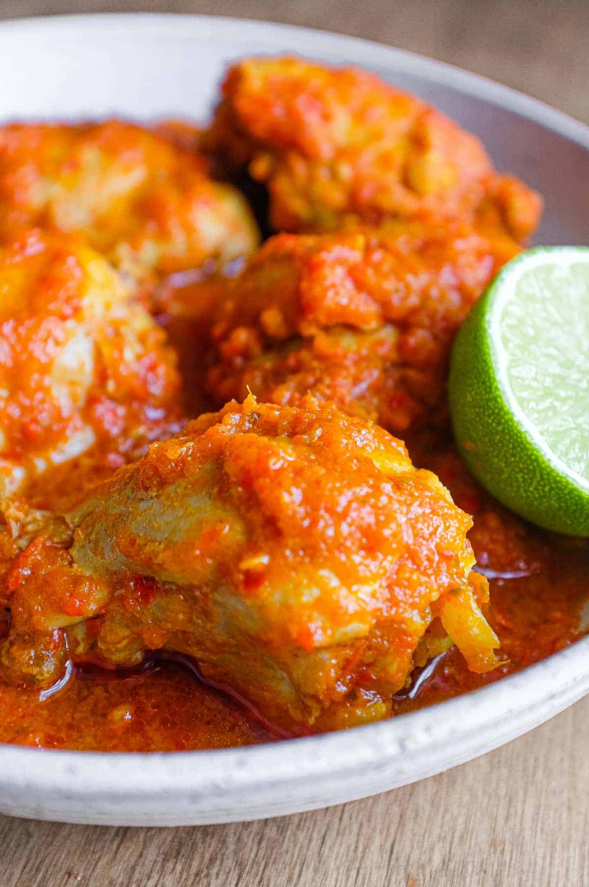 A bowl of Indonesian Ayam Rica Rica. A lime segment sits alongside as a garnish.