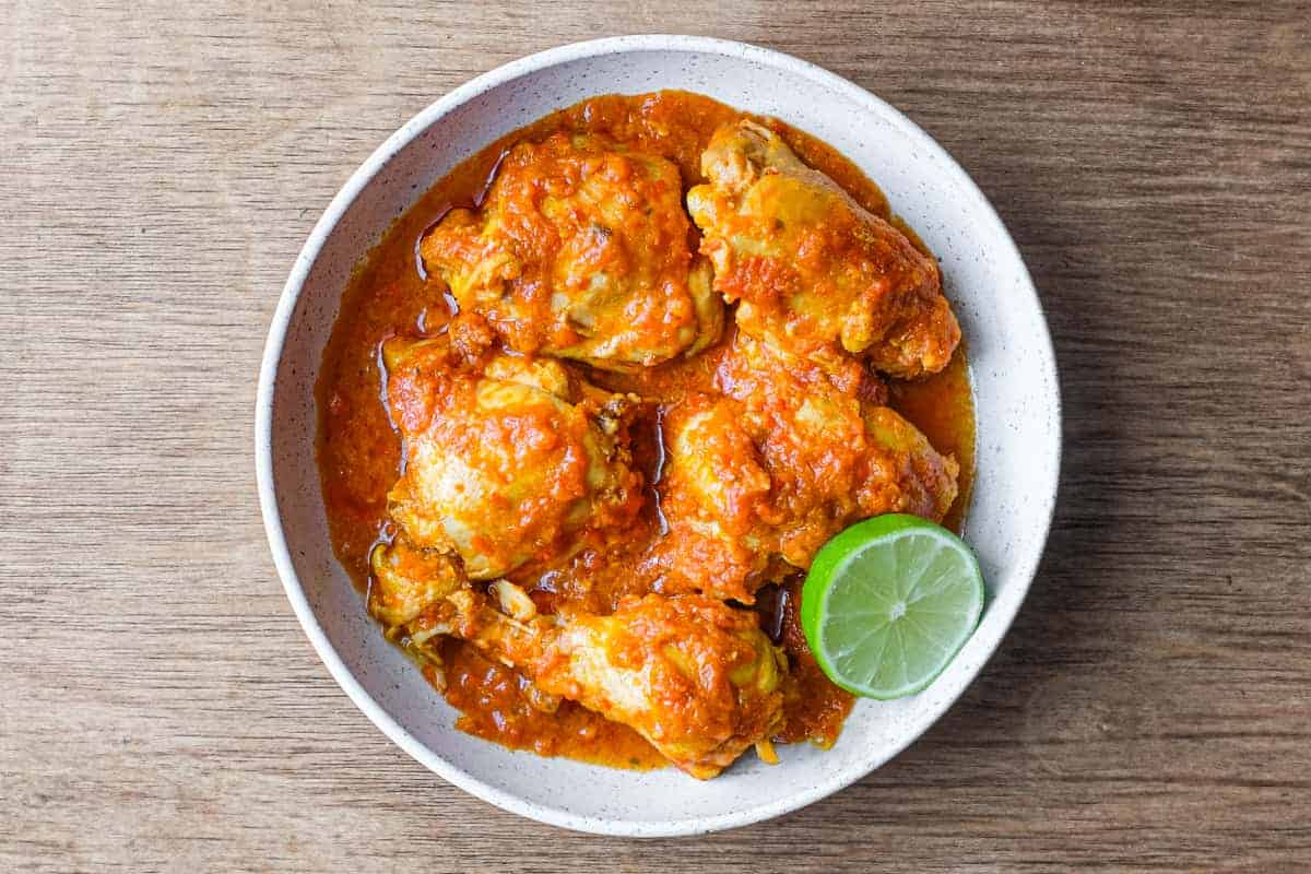 A bowl of Indonesian Ayam Rica Rica. A lime segment sits alongside as a garnish.