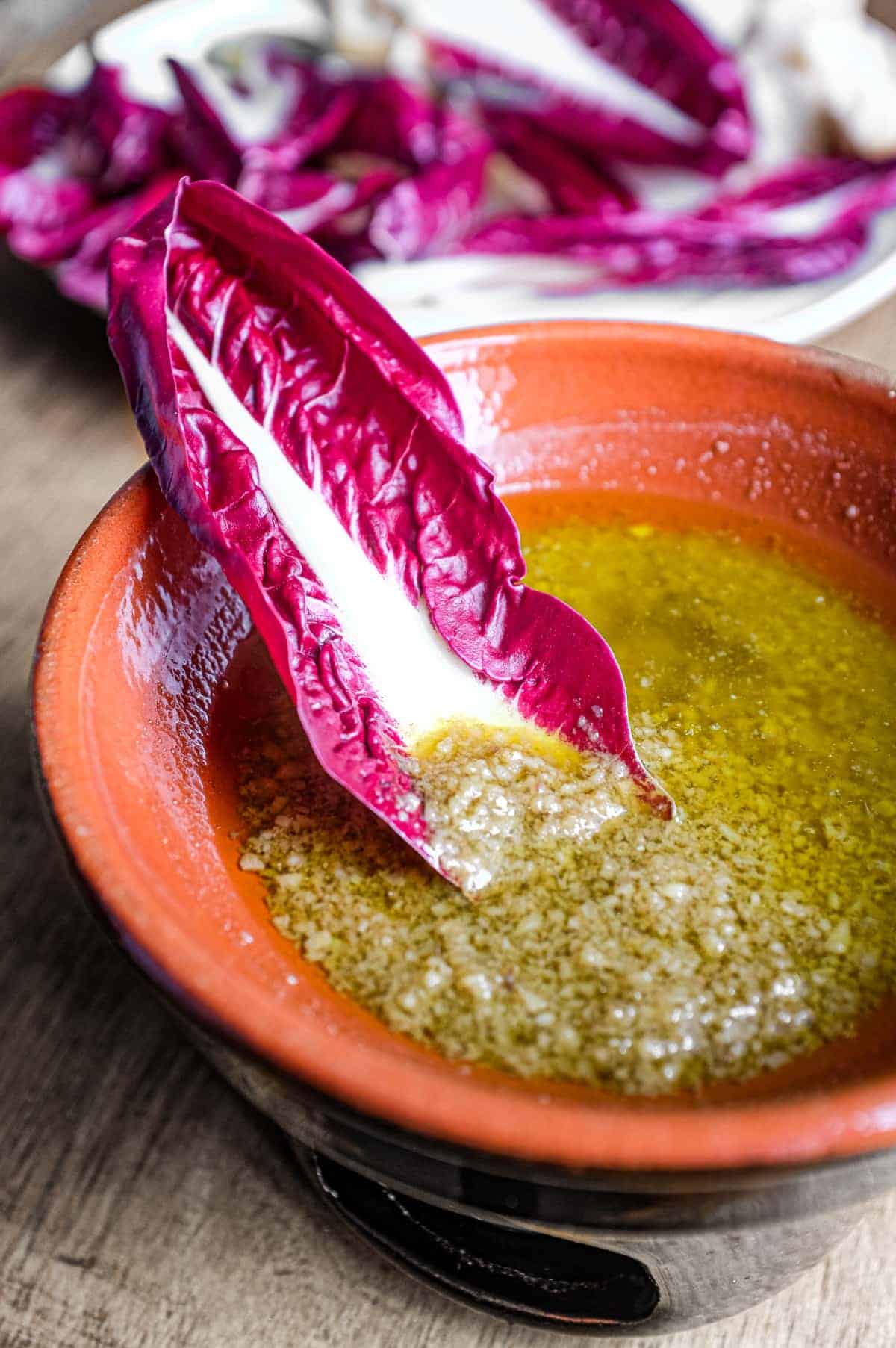 A small heated bowl of Italian Bagna Cauda sauce with a single radicchio leaf dipping into the sauce.