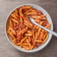 A bowl of nduja pasta sauce with penne pasta. A fork sits in the bowl too.