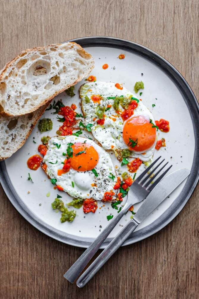 A plate with two fried eggs dotted with spicy Shatta chilli sauce. 