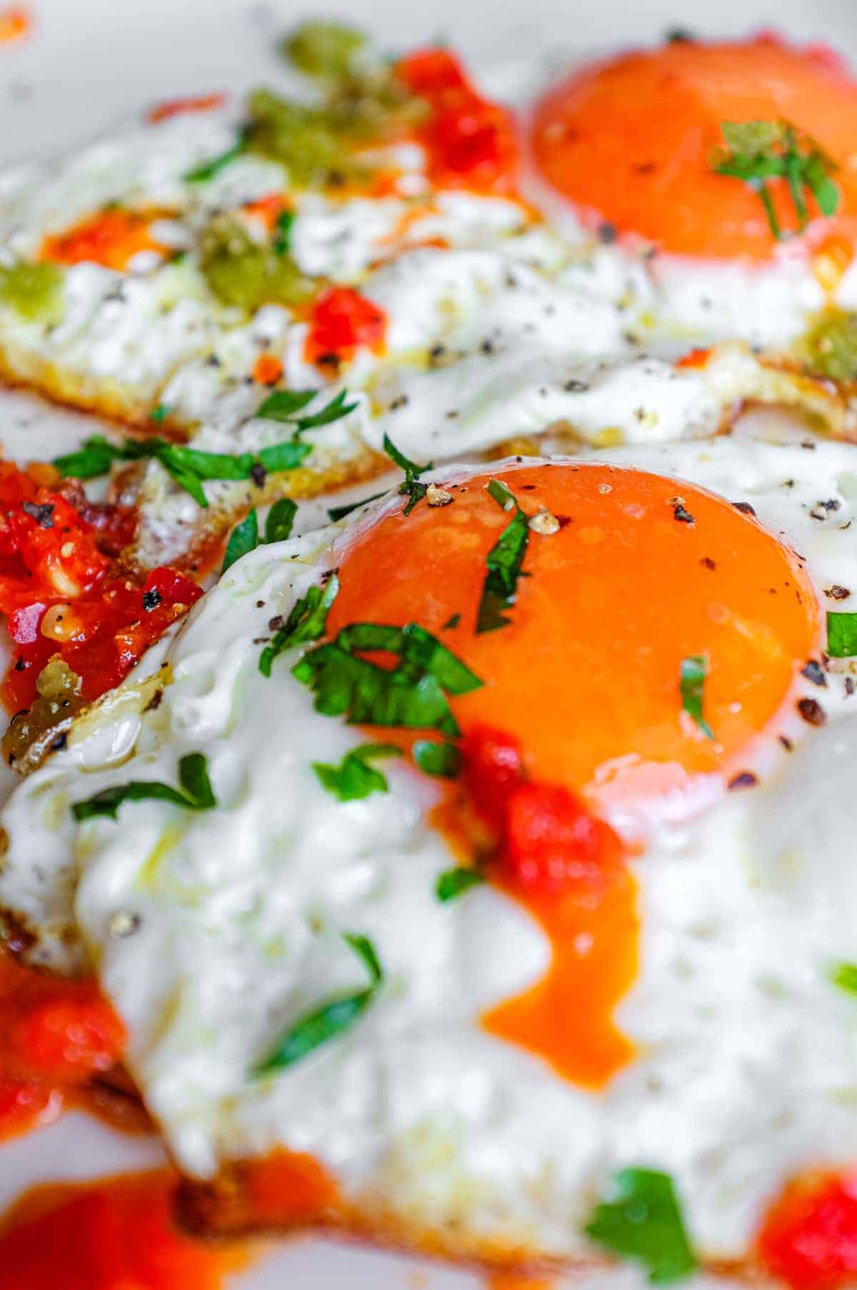 A plate with two fried eggs dotted with spicy Shatta chilli sauce. 