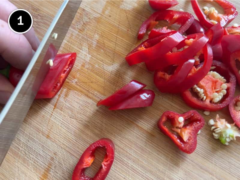 Chopping red chillies in a board into slices.