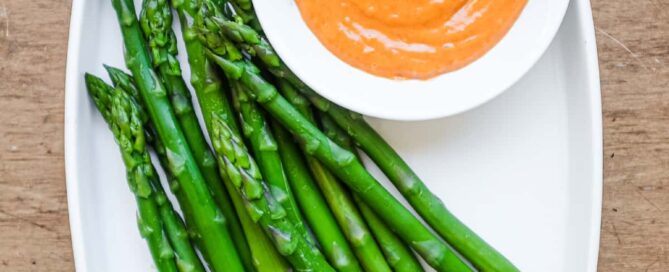 A small bowl of smoked alioli mayonnaise alongside some cooked asparagus