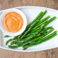 A small bowl of smoked alioli mayonnaise alongside some cooked asparagus