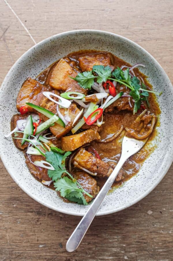 A bowl of Gaeng Hung Lay (Thai Pork Curry) garnished with herbs, spring onion, chilli and shallots