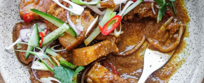 A bowl of Gaeng Hung Lay (Thai Pork Curry) garnished with herbs, spring onion, chilli and shallots