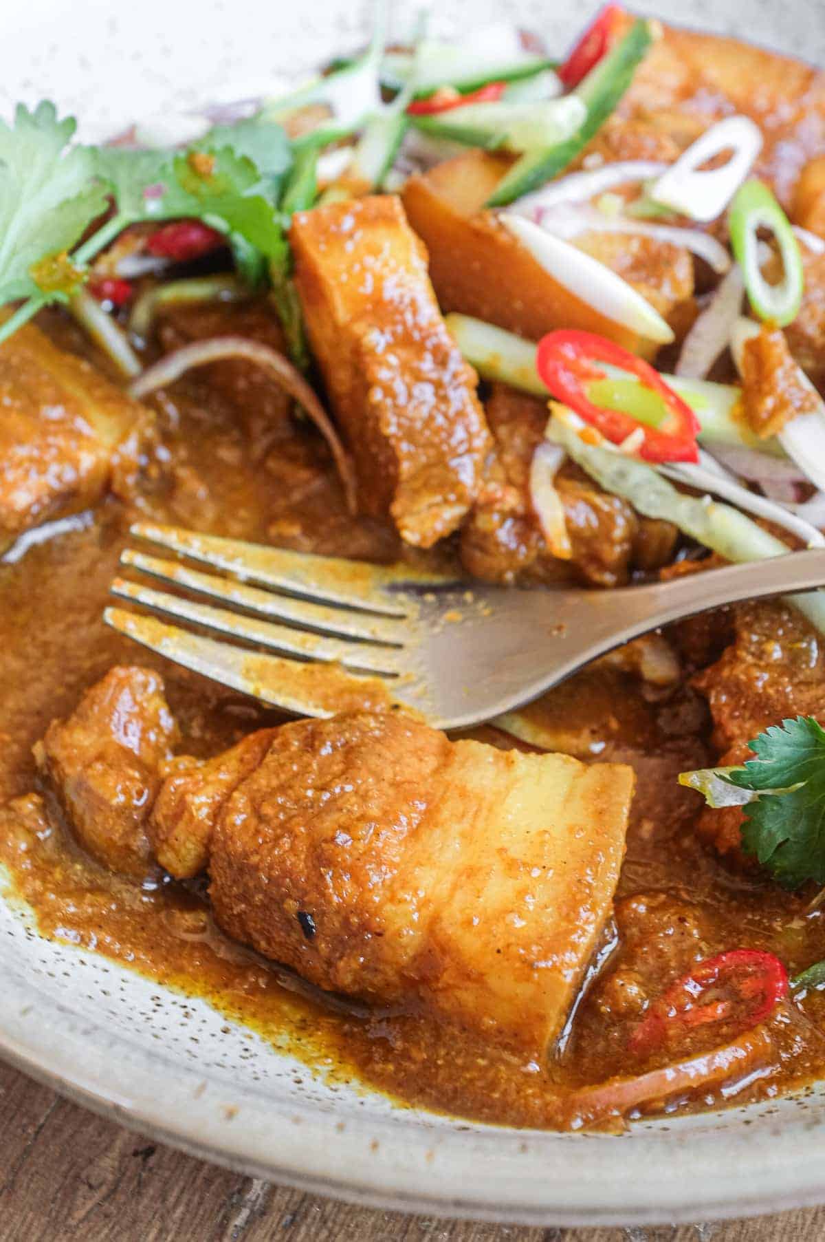 A bowl of Gaeng Hung Lay (Thai Pork Curry) garnished with herbs, spring onion, chilli and shallots