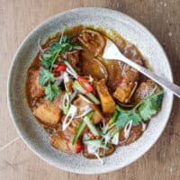 A bowl of Gaeng Hung Lay (Thai Pork Curry) garnished with herbs, spring onion, chilli and shallots