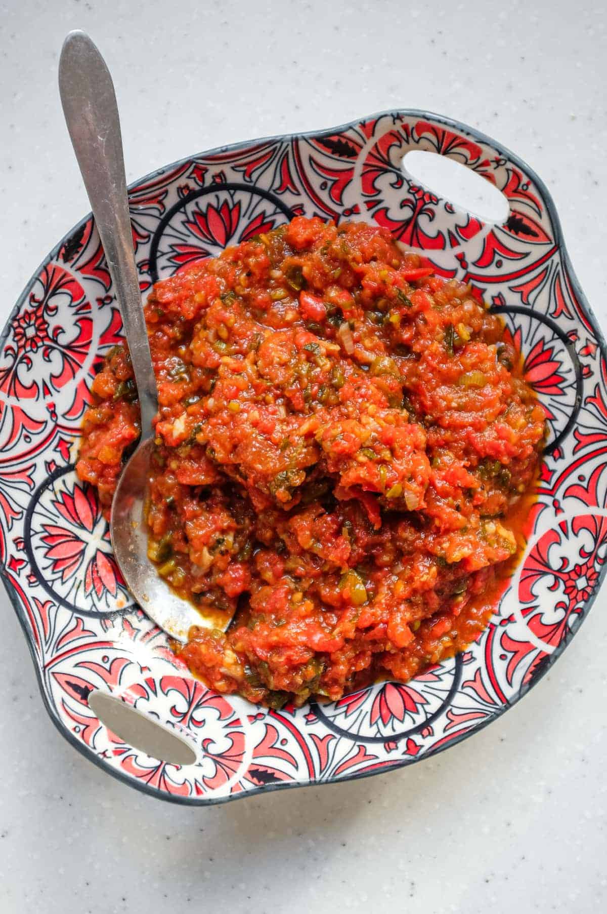 A bowl of Colombian Hogao sauce in a small patterned bowl with a serving spoon