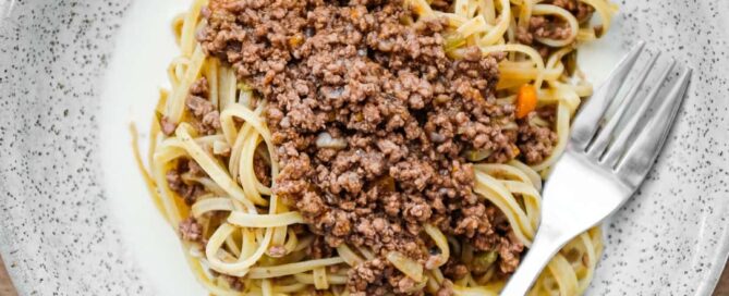 A small bowl of Tajarin pasta with meat sauce on a bed of cheese fondue sauce. A fork sits on the bowl.