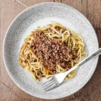 A small bowl of Tajarin pasta with meat sauce on a bed of cheese fondue sauce. A fork sits on the bowl.