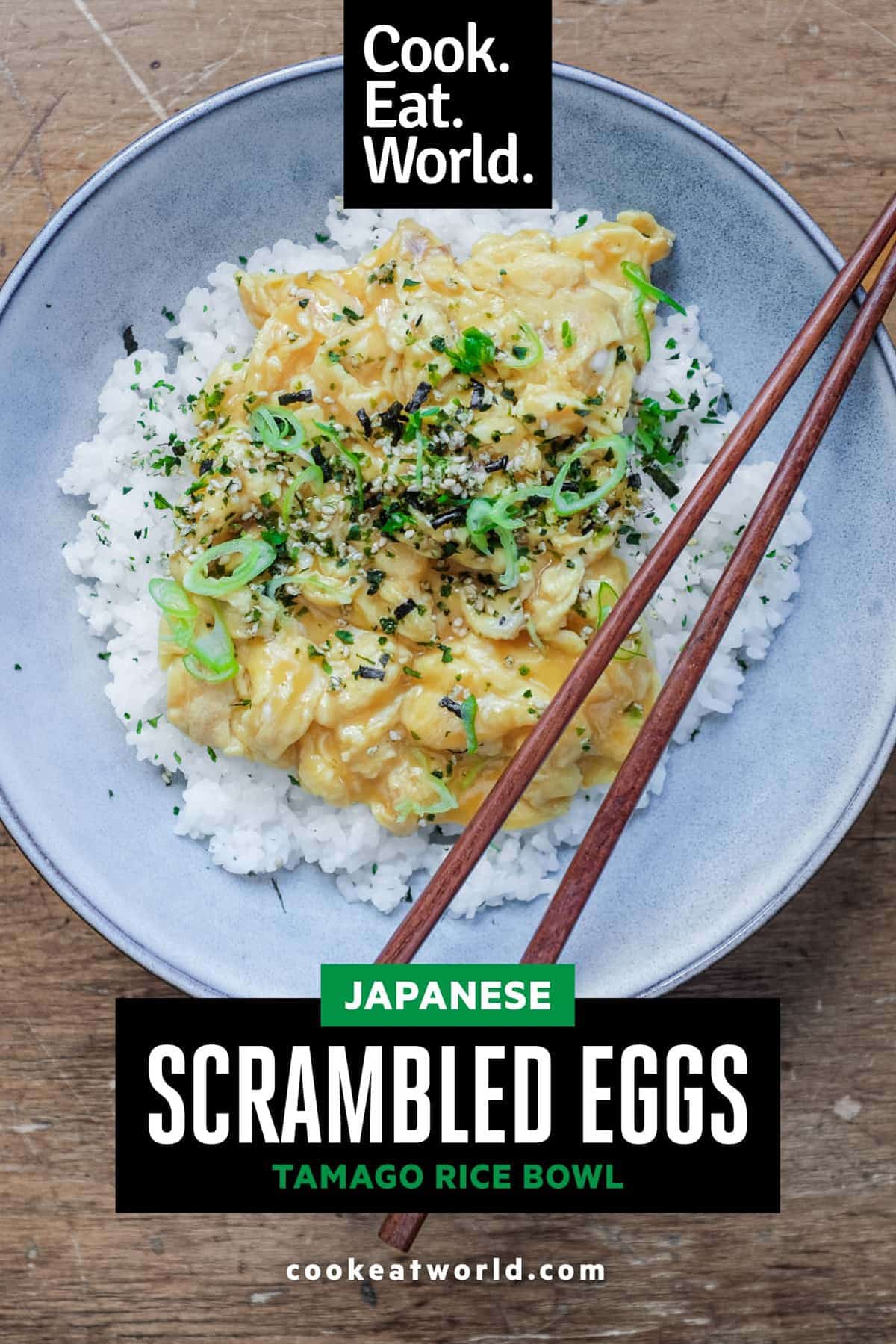 A bowl of Japanese scrambled eggs over rice and garnished with rice seasoning and spring onions. Wooden chopsticks sit on the bowl.