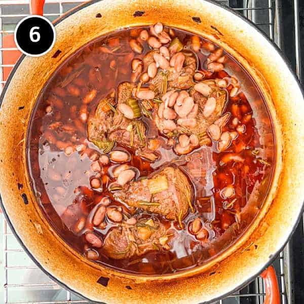 Lamb stewing in a pan with beans in an nduja sauce