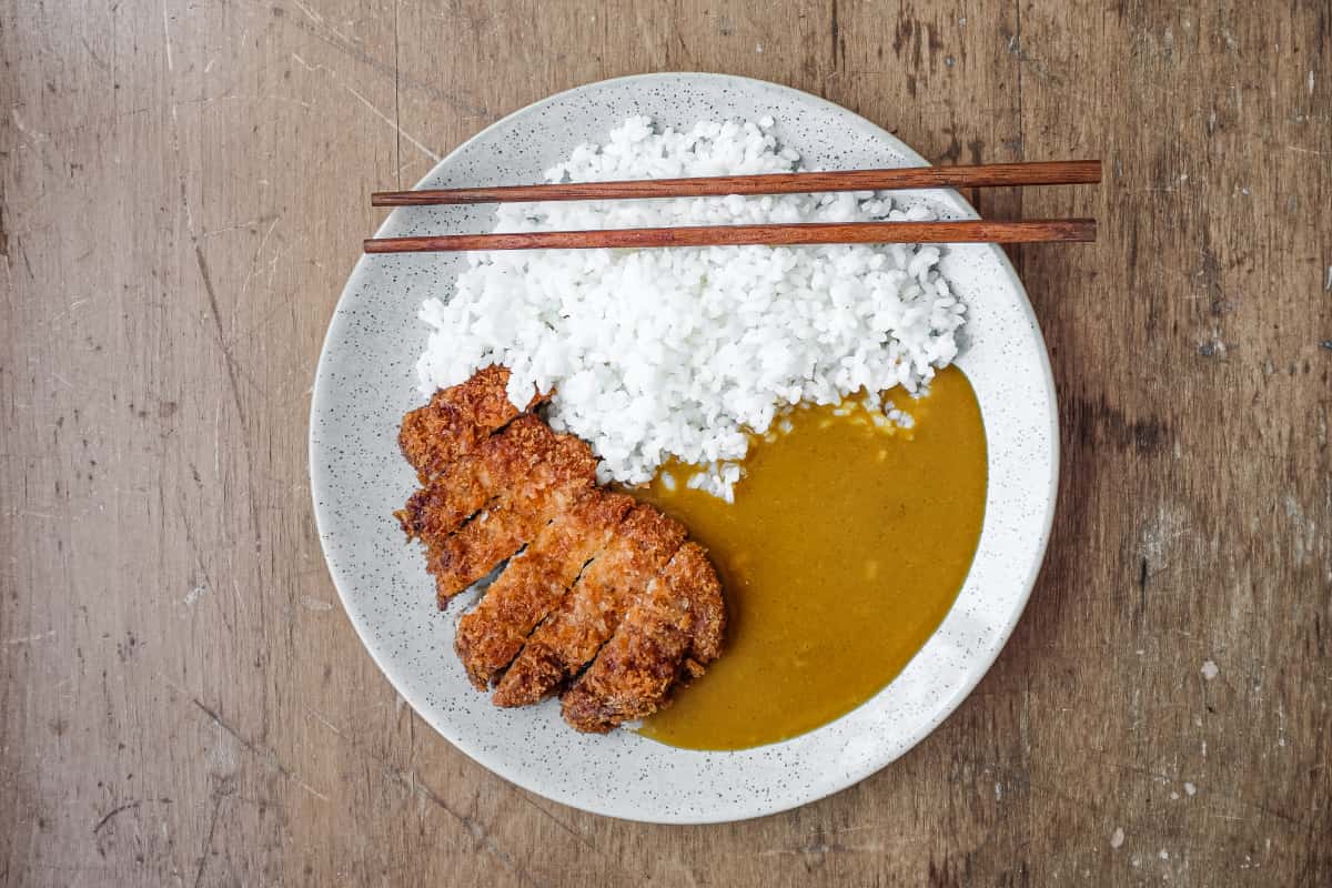 A plate of pork katsu with rice and curry sauce. Two chopsticks rest on the plate.