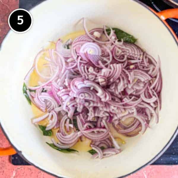 Andhra Chicken | cookeatworld.com Onions frying with curry leaves in a large cast iron pot.