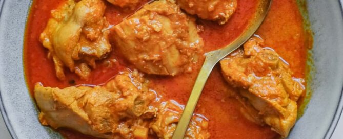 A small bowl of Indian chicken rogan josh curry with a serving spoon