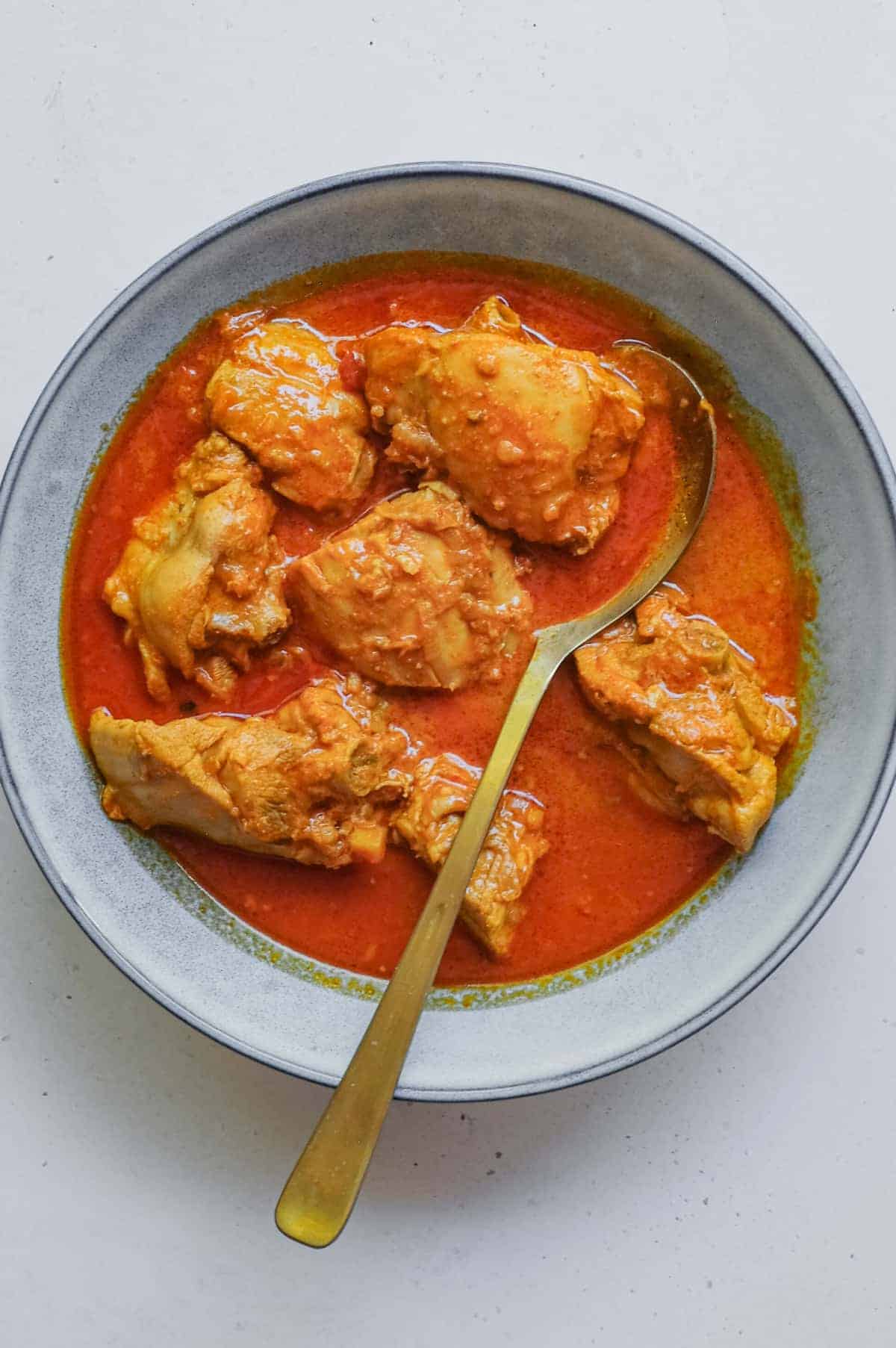 A small bowl of Indian chicken rogan josh curry with a serving spoon