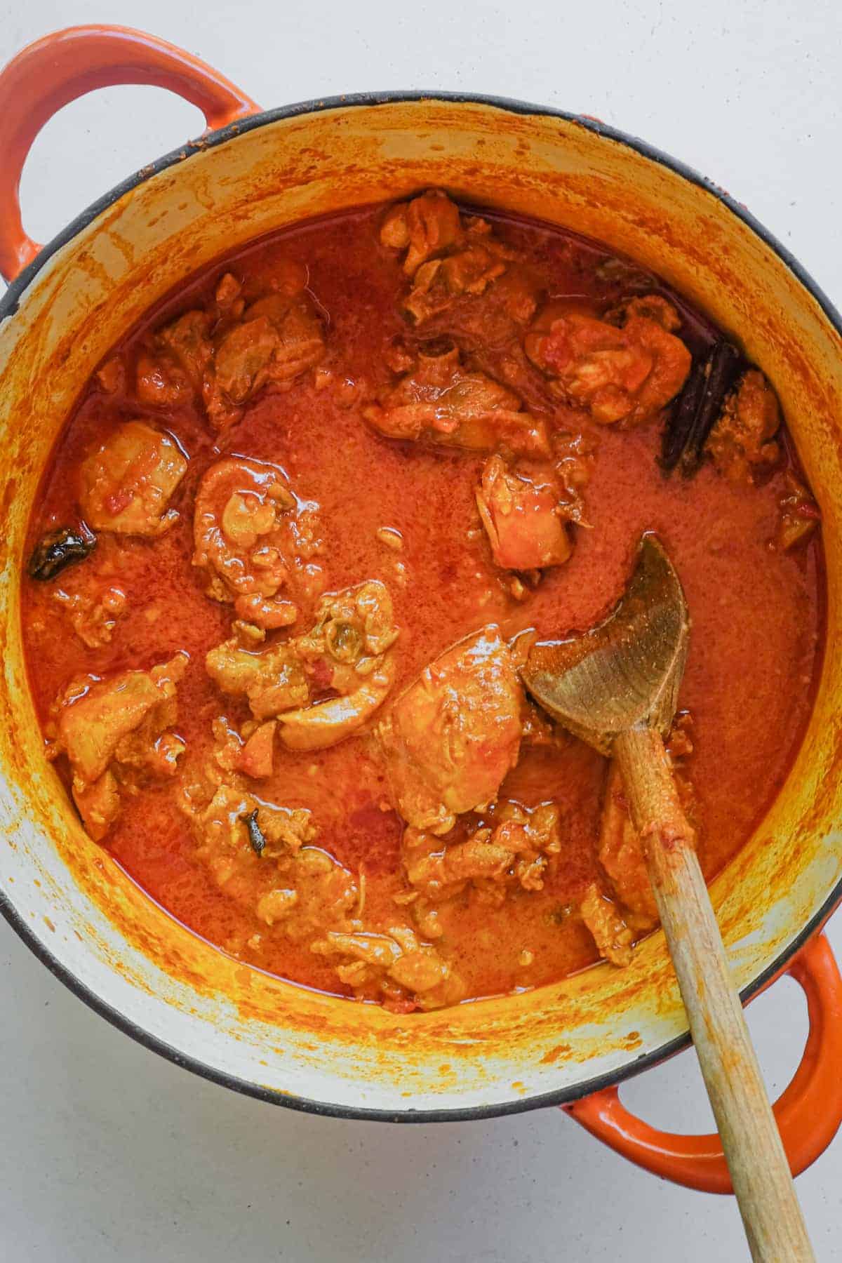 A pan filled with vibrant red chicken rogan josh curry, photographed from above.