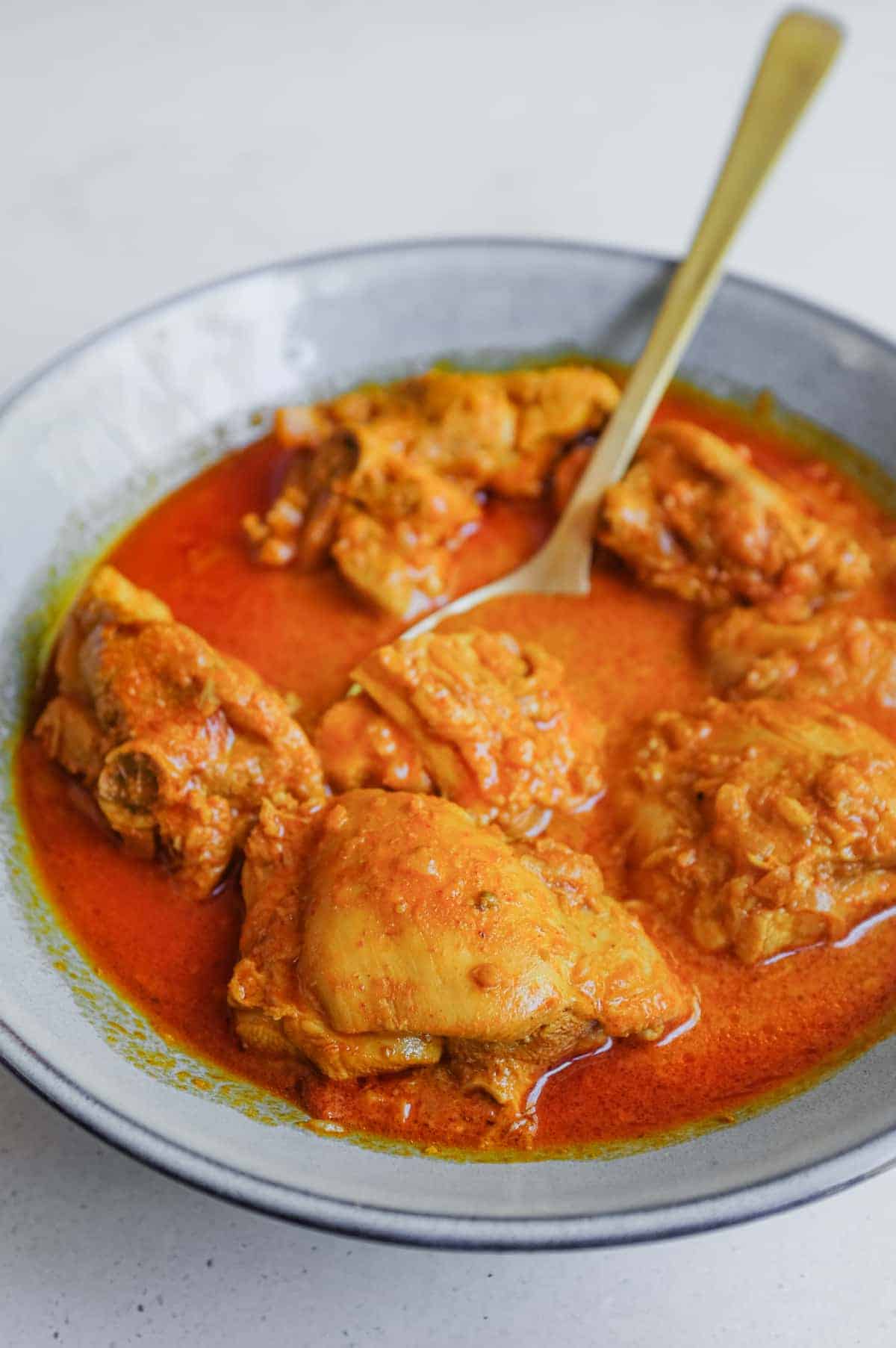 A small bowl filled with chicken rodan josh curry sits on an a stone work surface.