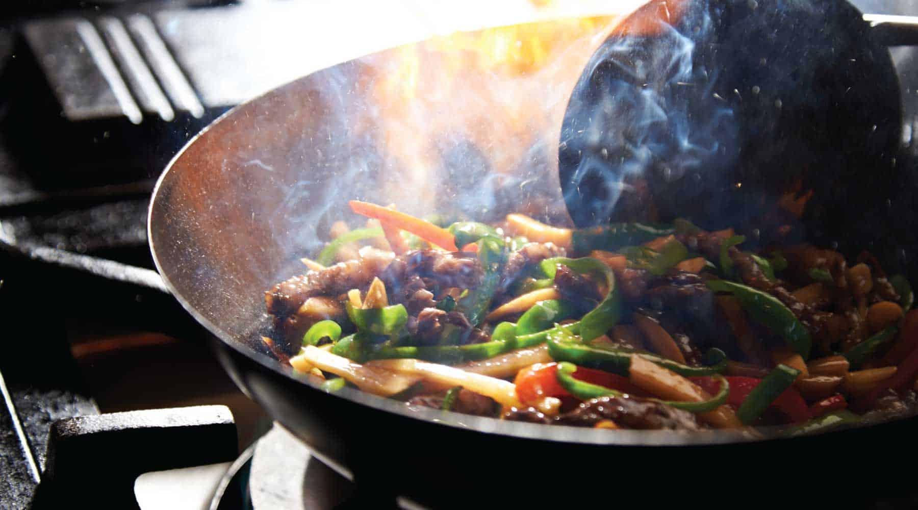 Beef and vegetable stir-fry cooking in a hot wok with rising smoke