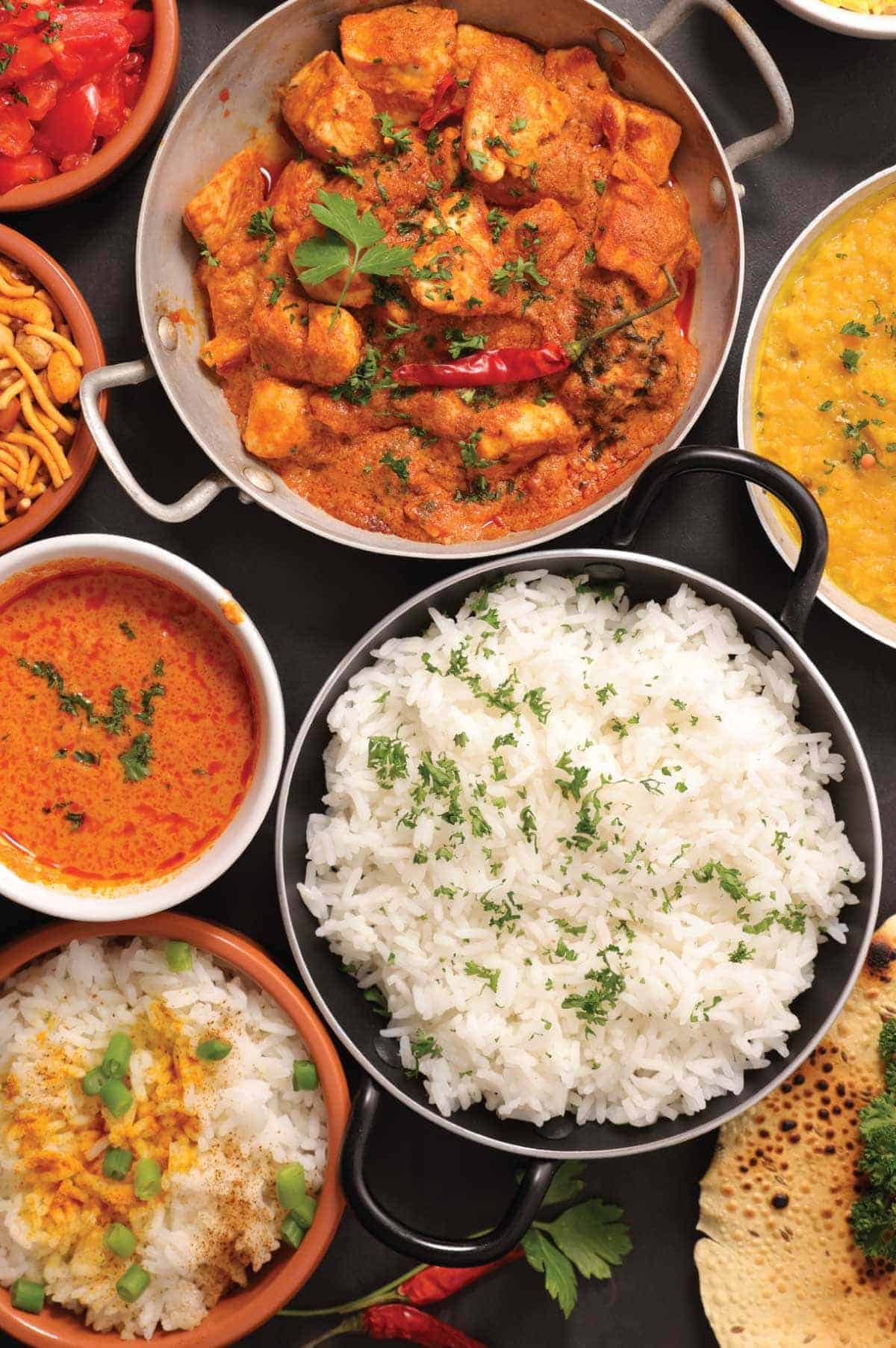 A vibrant overhead selection of Indian dishes including curries, rice, chutneys, and breads arranged together on a table.
