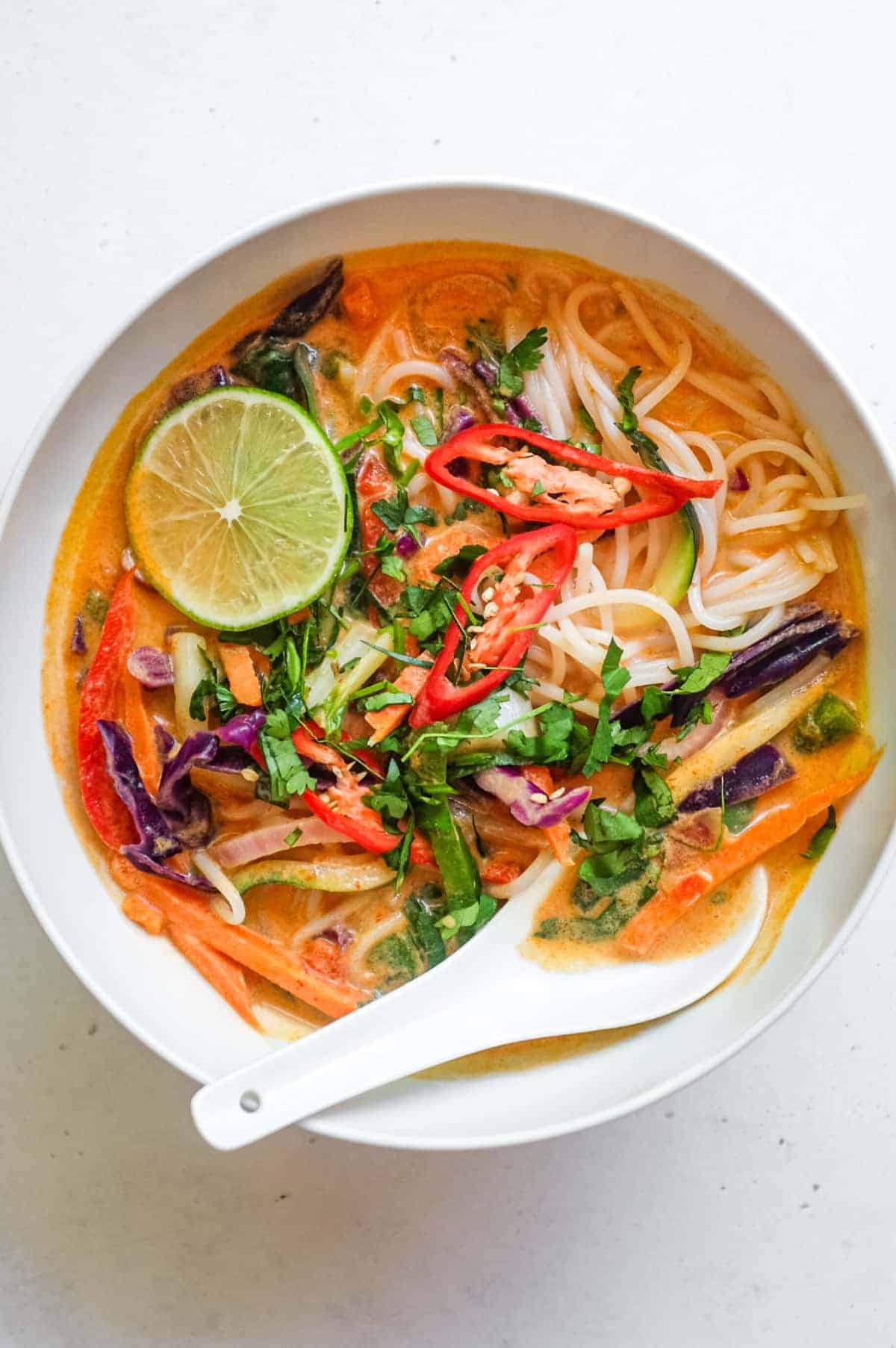 An overhead view of a bowl of Thai red curry noodles with fresh vegetables.