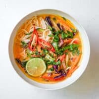 An overhead view of a bowl of Thai red curry noodles with fresh vegetables.