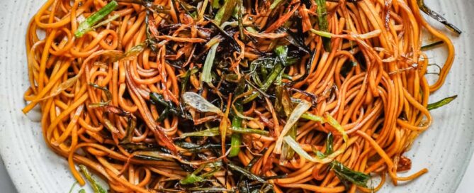 A hand serving a platter of Chinese scallion oil noodles.