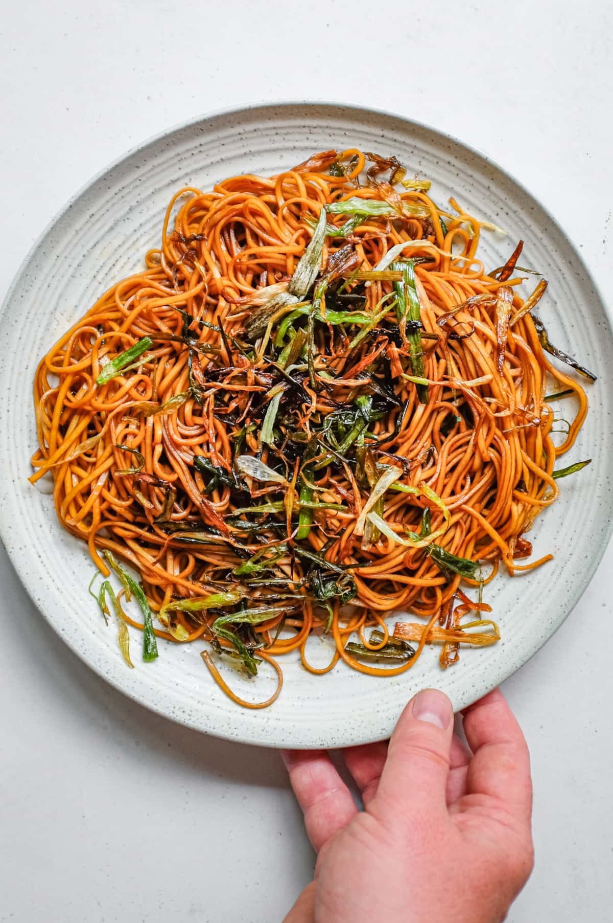 A hand serving a platter of Chinese scallion oil noodles.