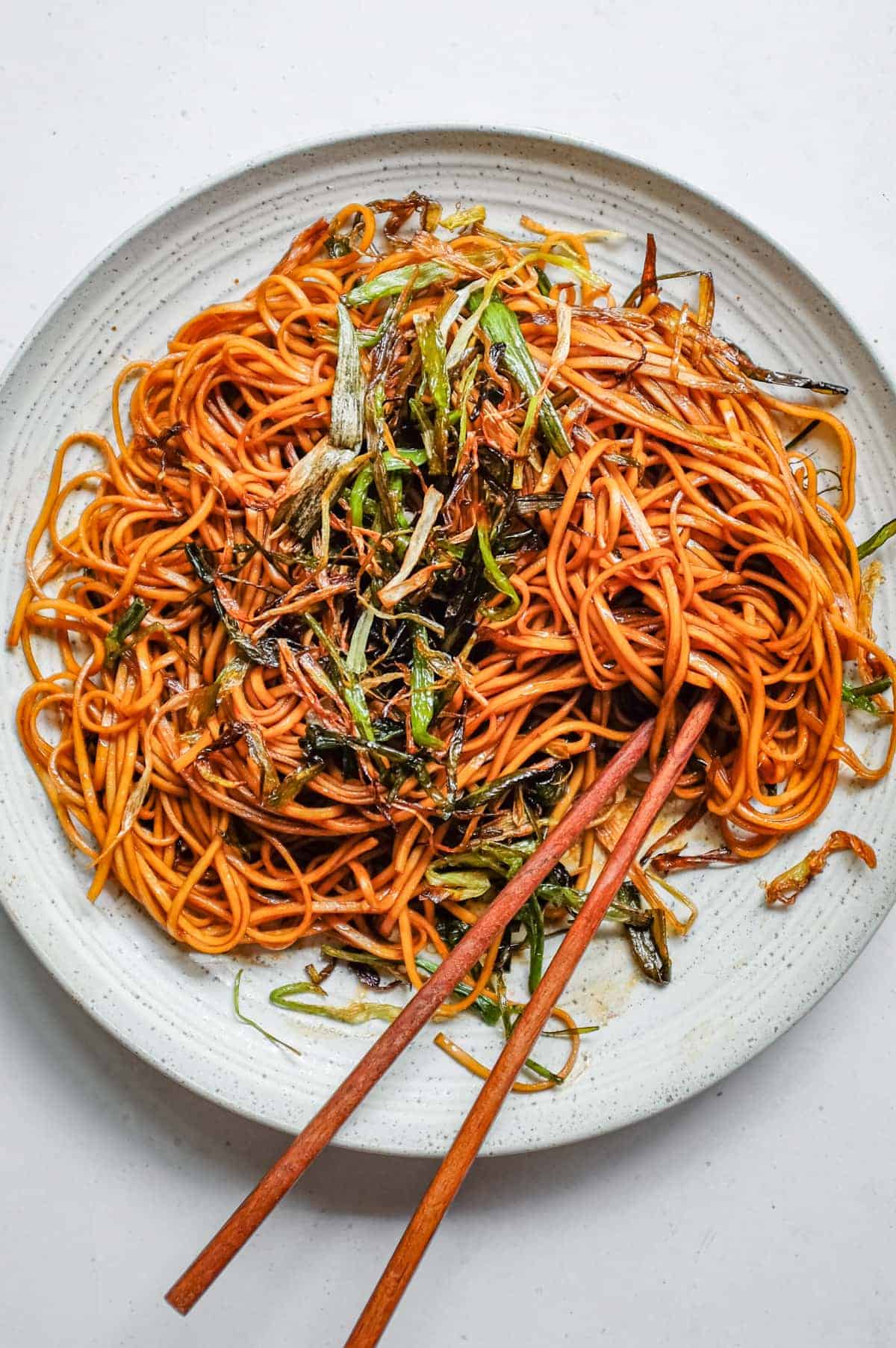 An overhead shot of a platter of Chinese scallion oil noodles with wooden chopsticks.