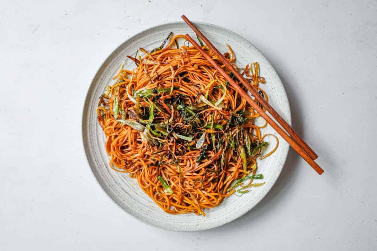 A platter of Chinese scallion oil noodles with some chopsticks.