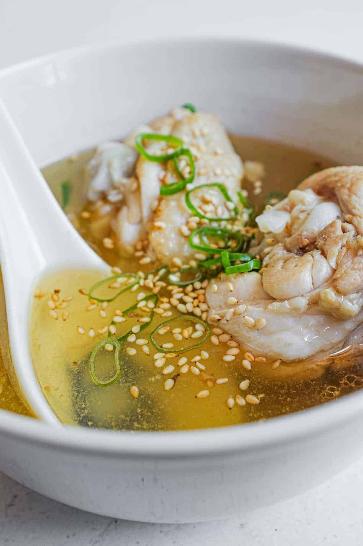 A close up of a bowl of Taiwanese Sesame Oil Chicken Soup, scattered with sesame seeds and spring onions.