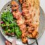A platter showing chicken kebab on bread with a side salad