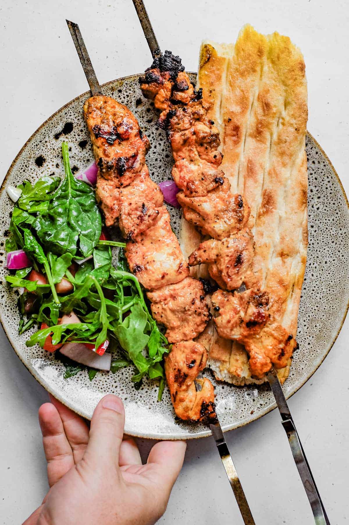 A platter showing chicken kebab on bread with a side salad