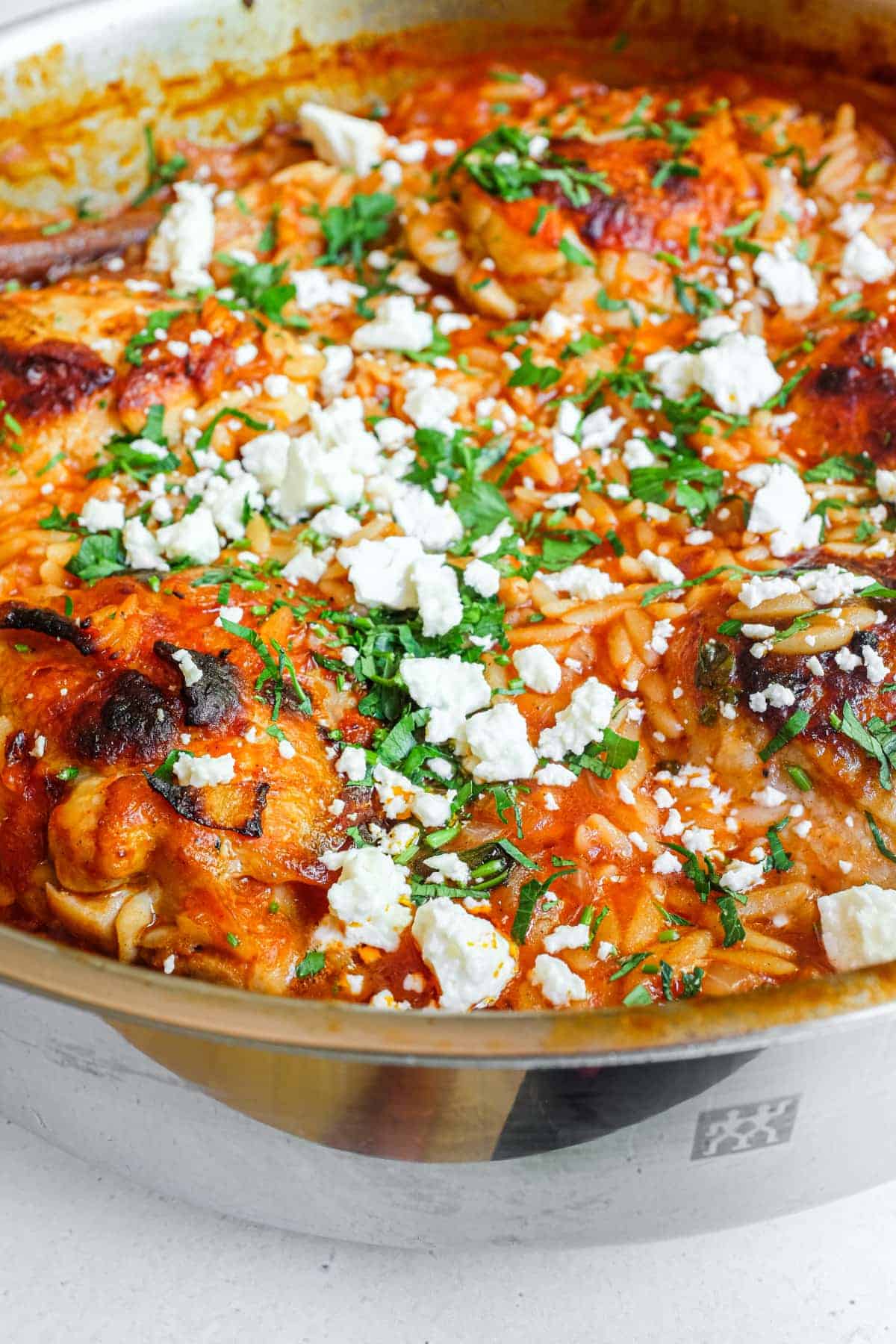 A side angle of a pan of Greek Youvetsi Chicken scattered with feta and fresh parsley.