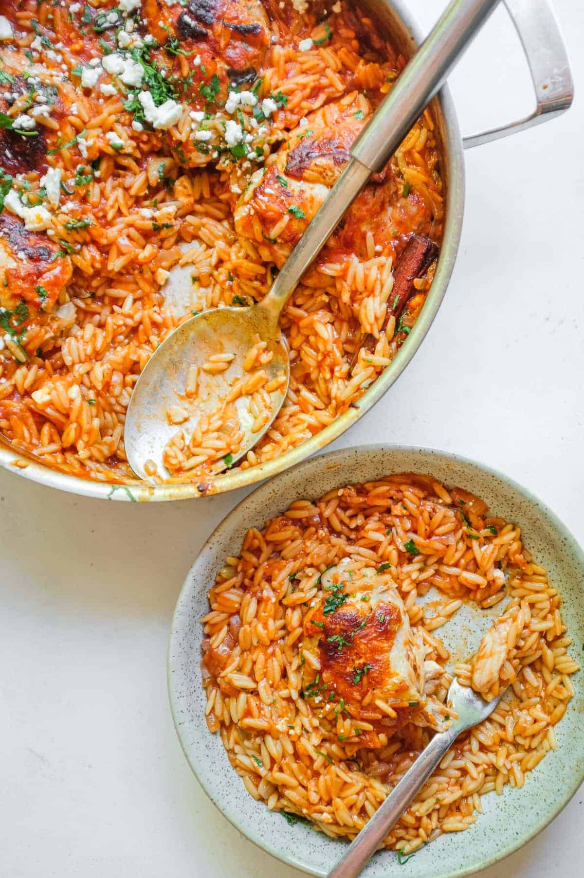 A pan and spoon sit nest to a small bowl of Greek Youvetsi Chicken.