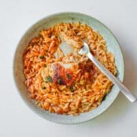 A small bowl and spoon with Greek Youvetsi Chicken (chicken and orzo).