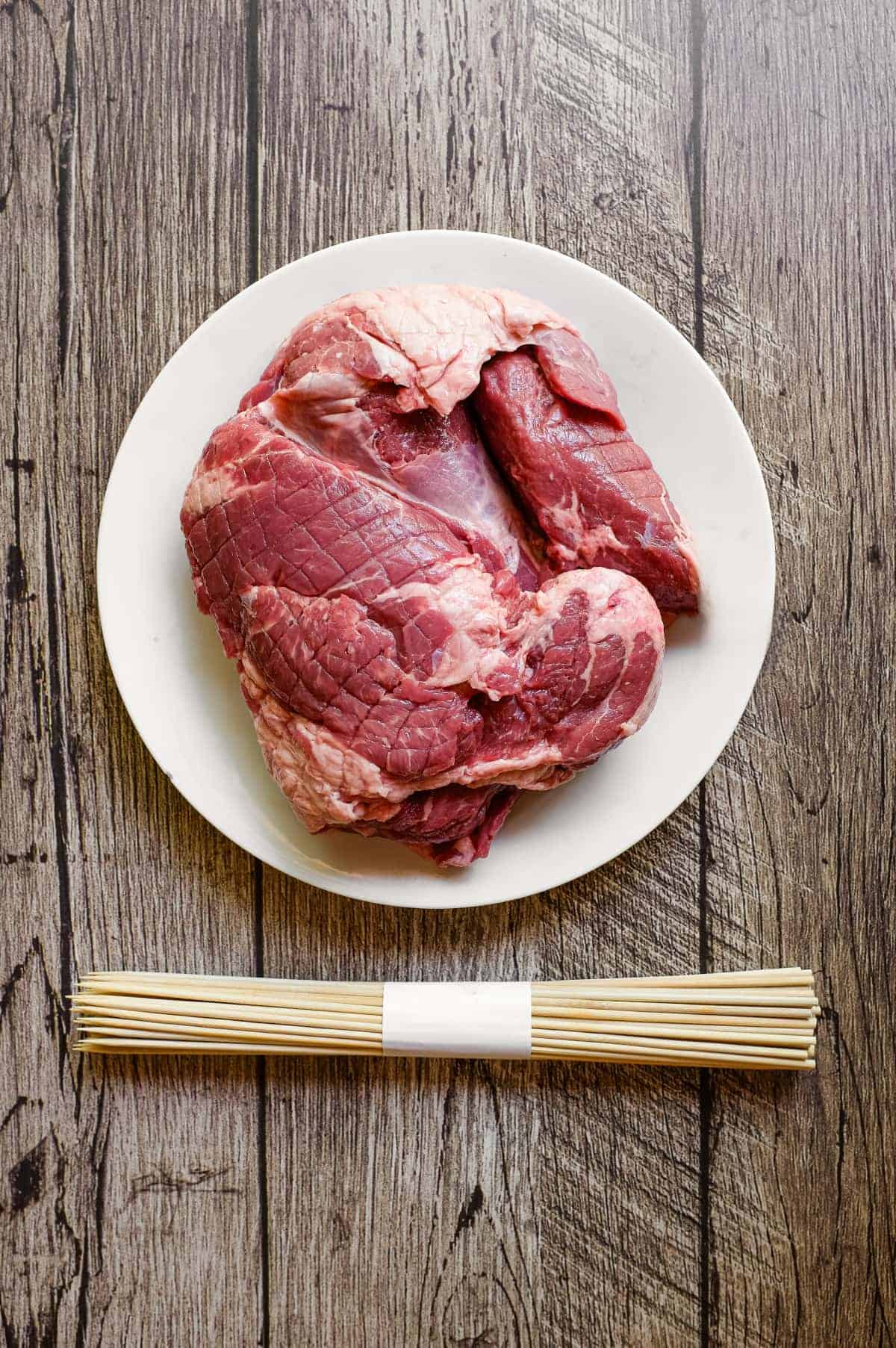 Arrosticini (Italian Lamb Skewers) | cookeatworld.com A lamb shoulder sits alongside a bundle of wooden skewers. Ready to make Italian arrosticini.
